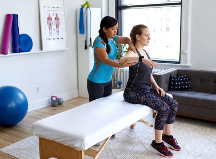 Female PT holds arm of patient in bright white room